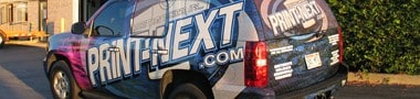 A car parked outdoors in IL is covered in a colorful vinyl wrap displaying "PRINTNEXT.COM" on its side and rear windows, showcasing expert vehicle wraps Spring Grove.