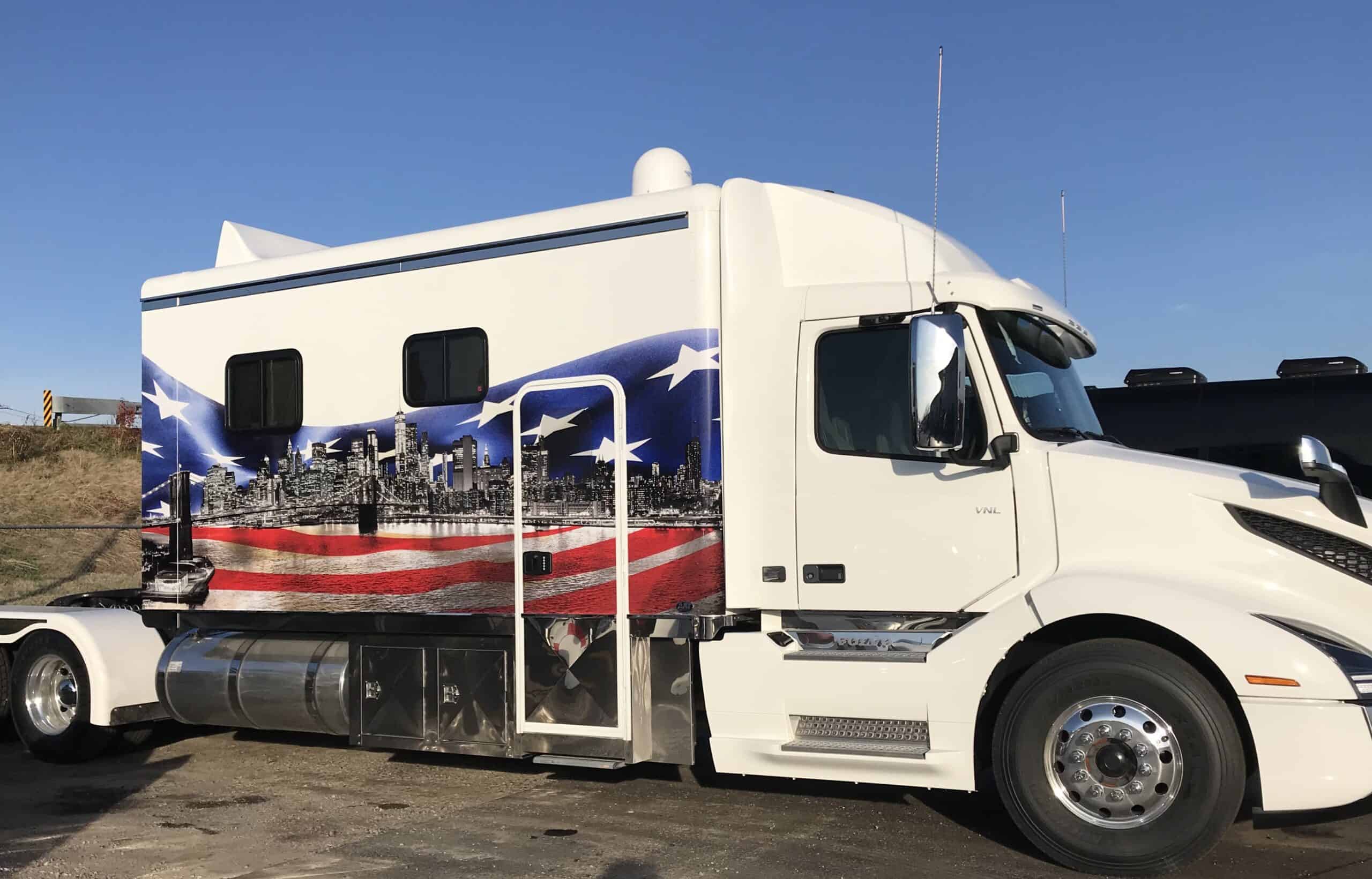 A white semi-truck with a mural on its side featuring the American flag and a city skyline under a clear blue sky, expertly designed with vehicle wraps Spring Grove, IL.