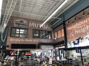 Interior of a hardware store with large wall signs reading "MUTUAL" and "Serving the North Shore Since 1917" above checkout counters—shelves display products, including materials for Car Wraps Spring Grove projects.