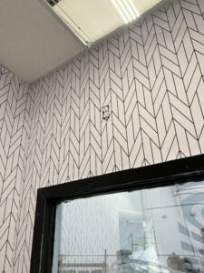 A wall with black and white herringbone-patterned wallpaper has an exposed electrical outlet near the ceiling. A black-framed window is visible at the bottom, offering a glimpse of Spring Grove, IL—home to standout vehicle wraps Spring Grove.