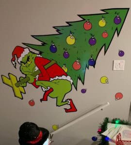 A wall decal of the Grinch in a Santa suit sneaking away with a Christmas tree, perfect for adding holiday cheer to your stairway. For more festive transformations, explore vehicle wraps Spring Grove, IL for your car this season!.