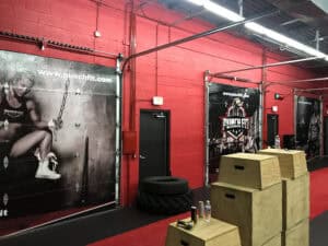 Interior of a gym in IL with red walls, large posters featuring athletes, stacked wooden plyometric boxes, water bottles, tires, and gym equipment on a vibrant red turf floor.
