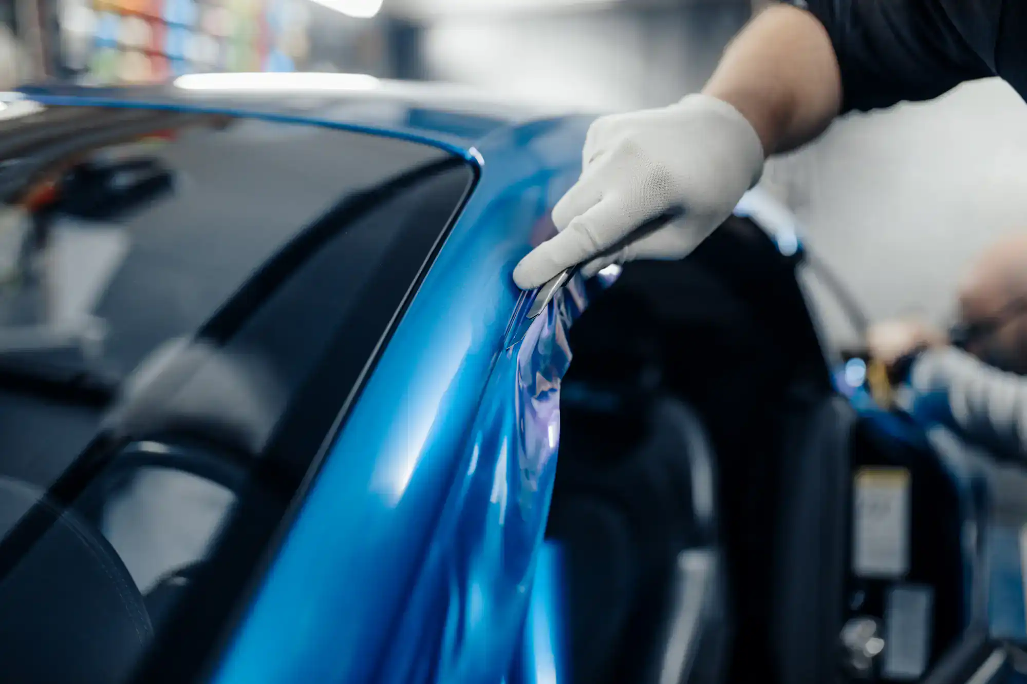A person wearing a white glove applies a blue vinyl wrap to the side of a car, carefully smoothing the material near the door and window—a precise process for top-quality Car Wraps Spring Grove.