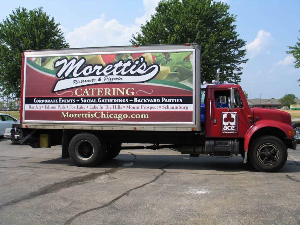 A red delivery truck with a large "Moretti’s Catering" advertisement on the side, promoting corporate events, parties, and listing various Chicago suburbs. The Moretti's website is displayed on the truck.